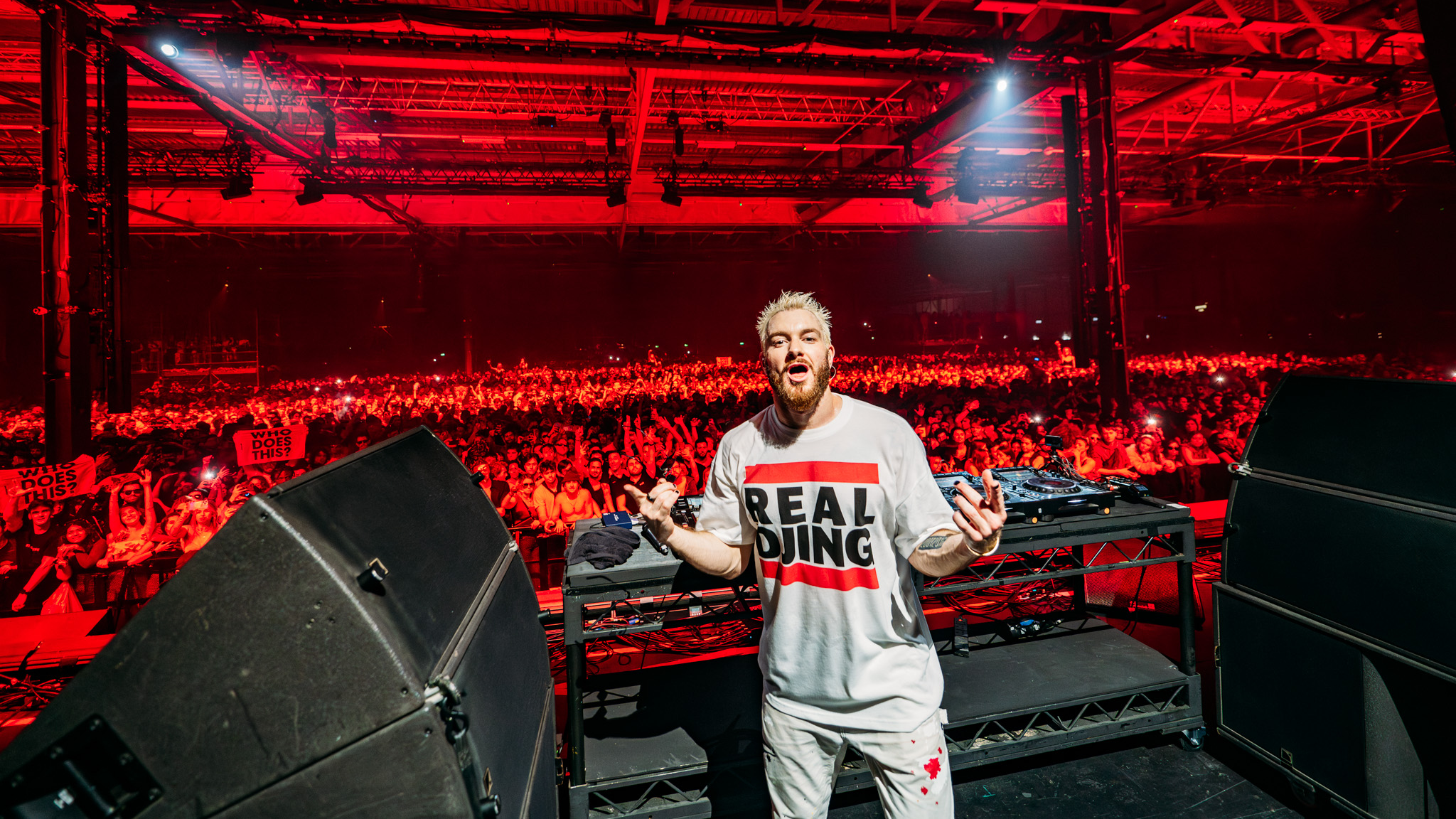 James Hype performing for a packed arena crowd under red lights.