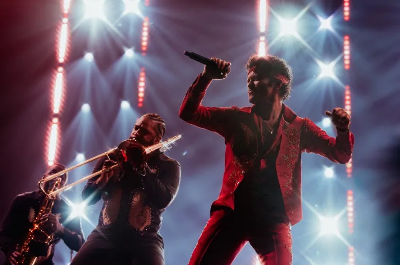 Bruno Mars performing with his band in a red outfit