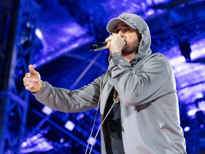 Eminem performing on stage in profile, pointing into the crowd with a microphone in hand