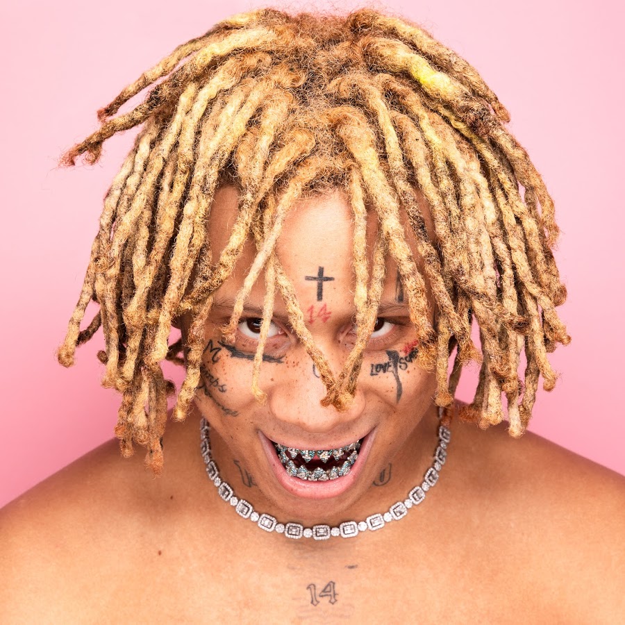 Trippie Redd smiling with braided hair and diamond chain against pink background